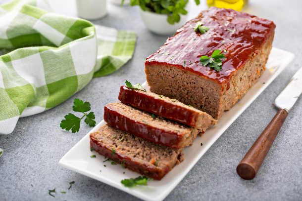 Loaf of meatloaf sliced and whole on serving platter with parsley and green and white kitchen towel - Instant Pot Meatloaf