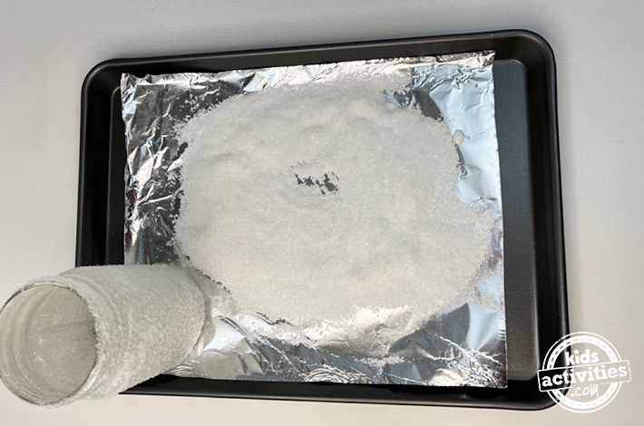 Craft Christmas - kids activities blog - step 2- Using a tray with aluminum foil on top, pour a lot (and we mean, a lot) of Epsom salt. Act quickly and roll the jar in the Epsom salt, pushing down slightly. Roll as many times as needed to ensure every space has been covered.