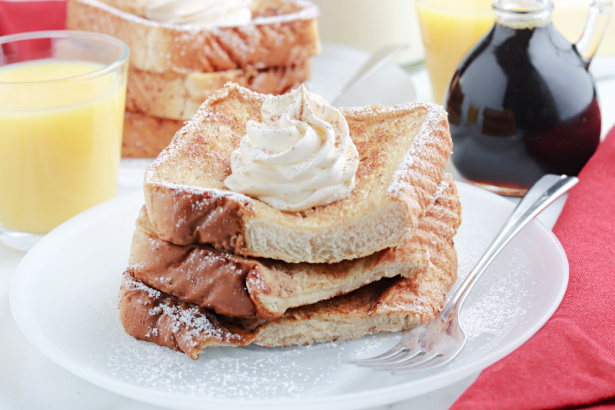 Easy Eggnog French Toast - a white plate with Eggnog French Toast, topped with whipped cream and powdered sugar, with orange juice and maple syrup in the background- Kids Activities Blog 