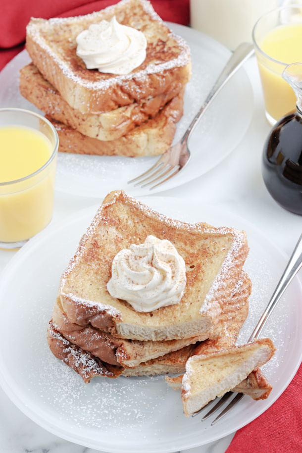 Easy Eggnog French Toast - White plate with Eggnog French Toast sprinkled with powdered sugar and a dollop of whipped cream, with a glass of orange juice, and a red napkin - Kids Activities Blog