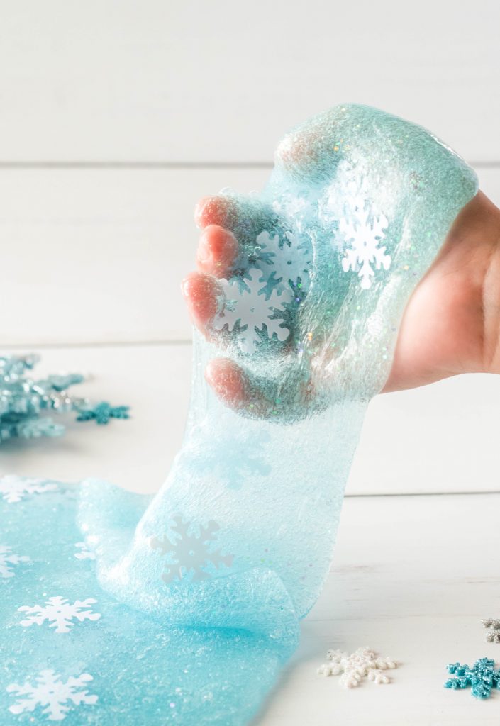 Blue slime being stretched in a hand with glitter with blue and white snowflake sequin