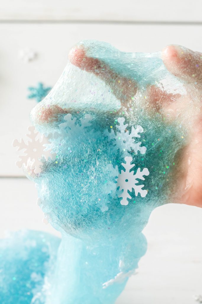 Blue slime being stretched in a hand with glitter with blue and white snowflake sequin