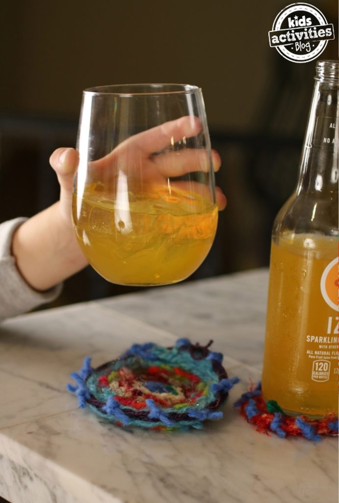 ideas for christmas homemade gifts- Image shows a kids' hand holding a glass with orange juice on top of a handmade coaster.