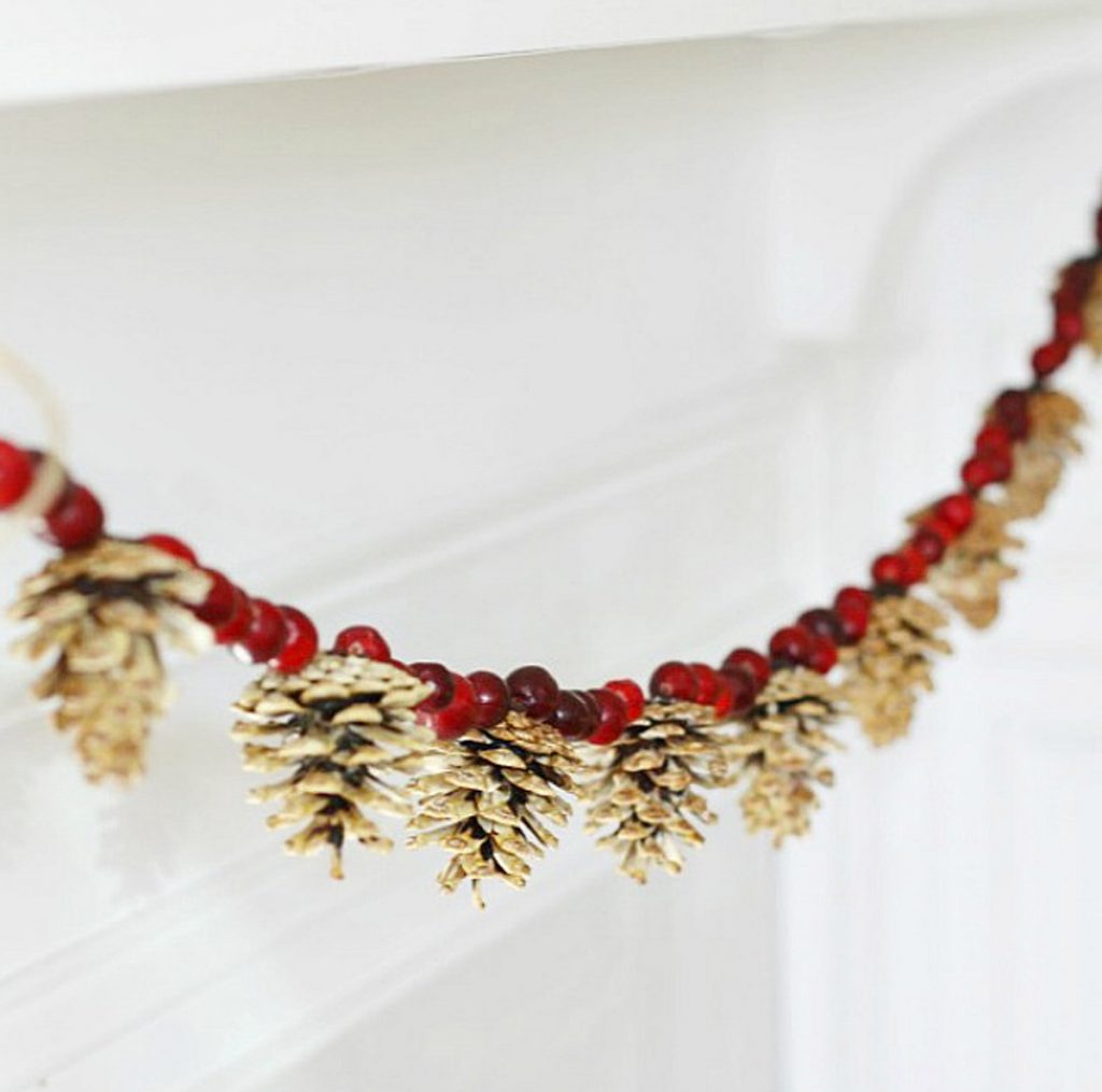 natural Christmas ornaments- Image shows a pinecone and cranberry garand hanging from a wall.