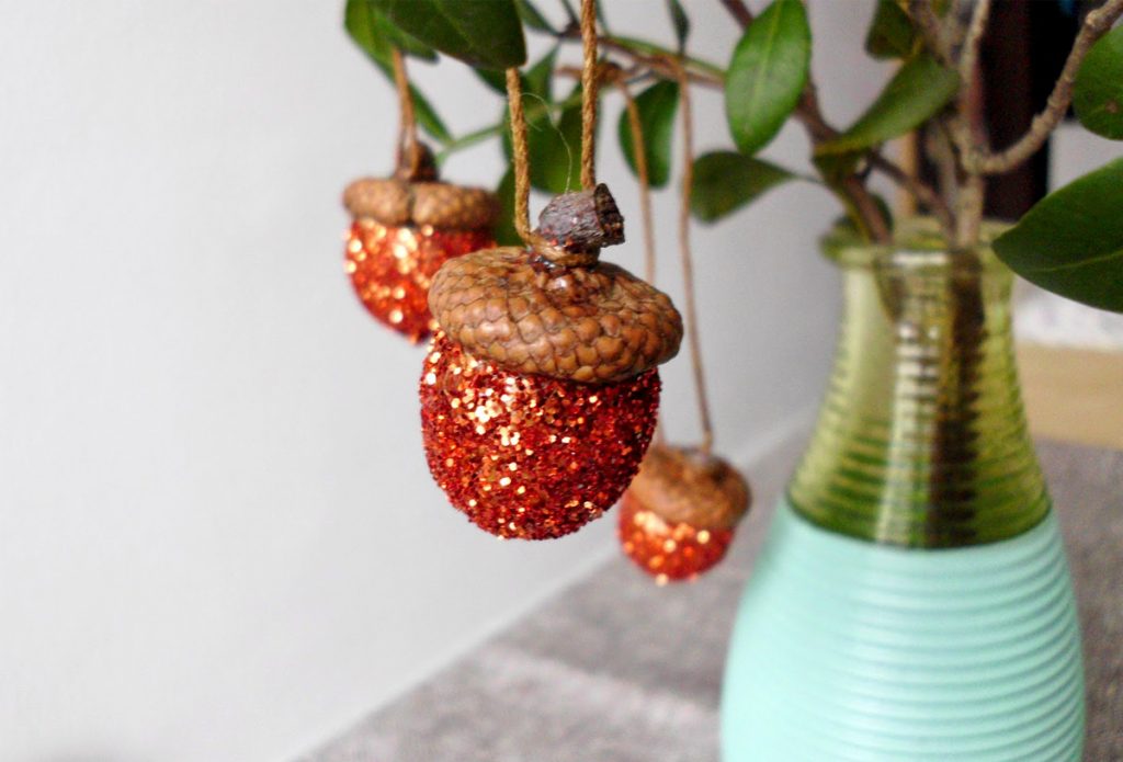 natural Christmas ornaments- Image shows glitte acorn ornaments hanging from a plant in a vase.