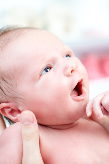 newborn baby held by adult looking up